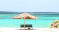 A bench on a sandy beach with a thatched umbrella.