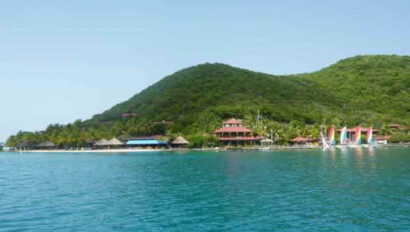 A small island in the middle of the ocean with sailboats on it.