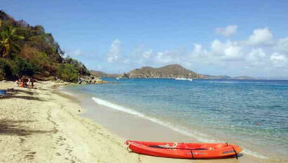 A red canoe sits on the shore of a beach.
