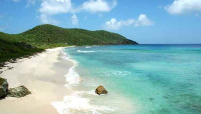 A sandy beach with blue water and green hills.