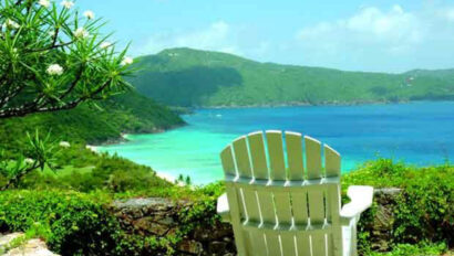 A white chair sits on a hill overlooking the ocean.