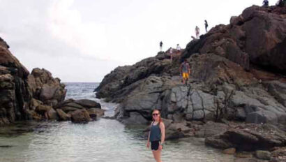 A woman standing on a rocky beach near a group of people.