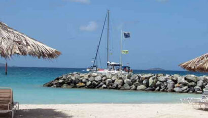 A beach with chairs, umbrellas, and a sailboat.