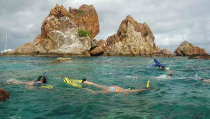 A group of people snorkling in the water near a rock formation.