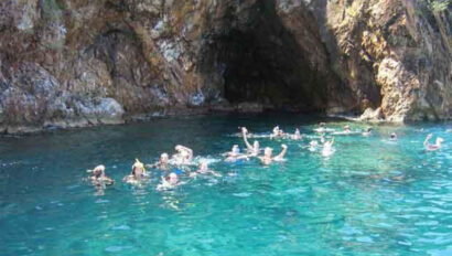 A group of people swimming in the water near a cave.