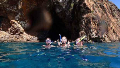Three people snork in the water near a cave.