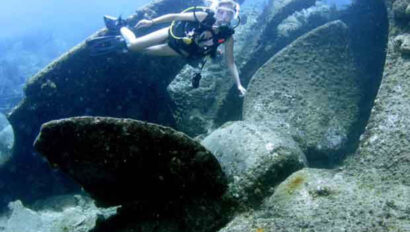 A woman is scuba diving near a large shipwreck.