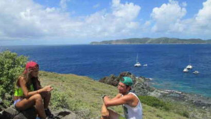Two people sitting on a rocky hill overlooking the ocean.