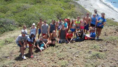 A group of people posing on top of a hill near the ocean.