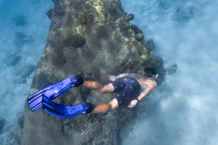 A man snorkling in the water near a rock.