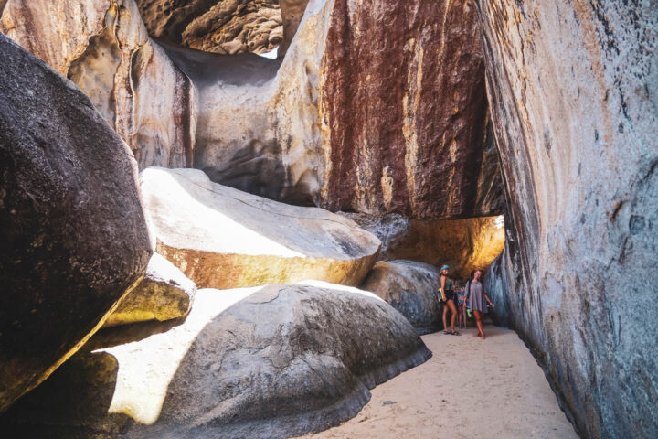 Two people walking through a narrow passage in a rock formation.