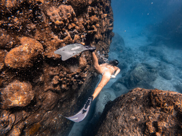 A woman snorkling in the water near a rock.