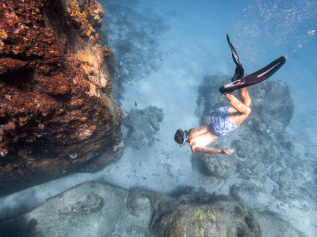 A man is snorkling in the water near a rock.