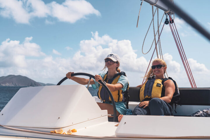 Two women are driving a sailboat in the ocean.