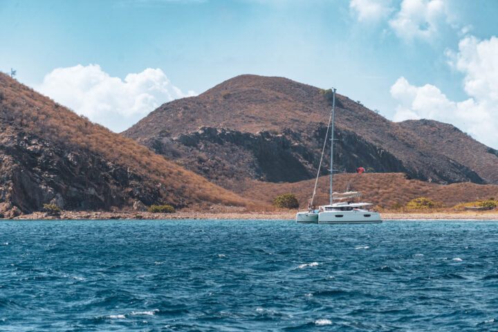 A catamaran sails in the ocean near a hill.