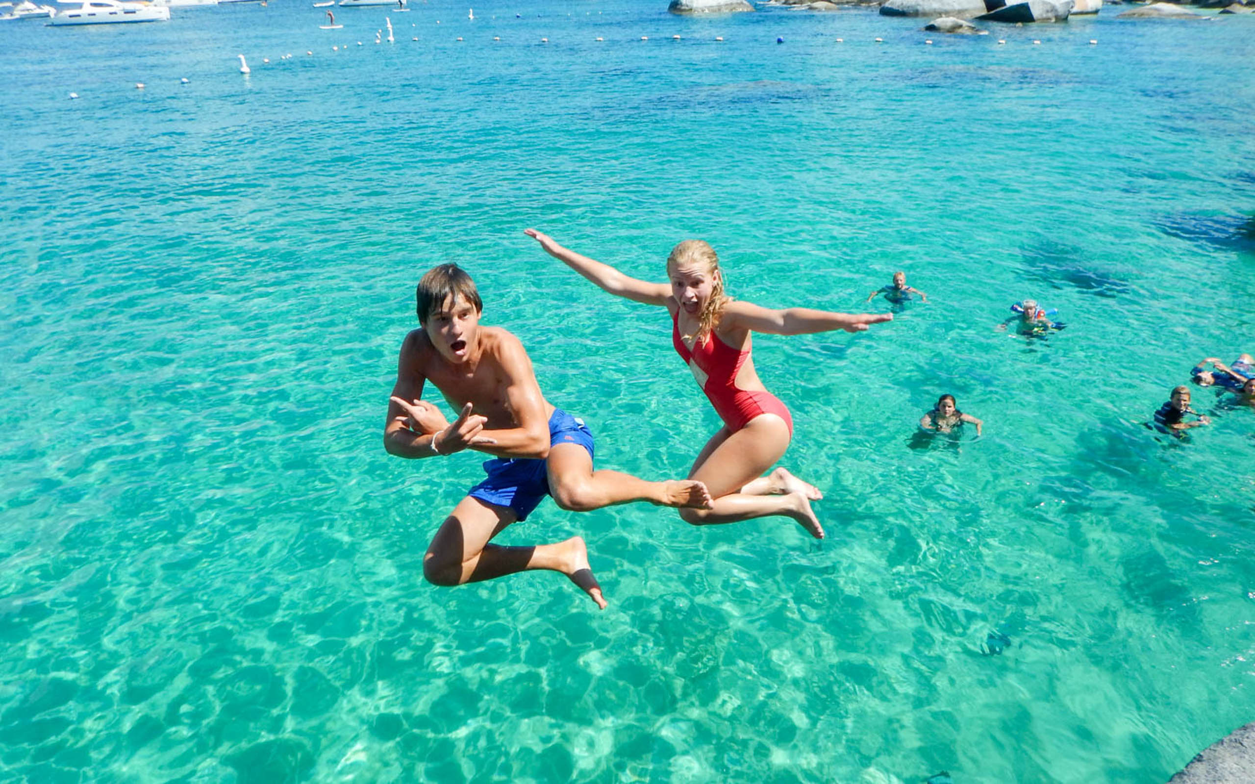 Two people jumping into the clear blue water.