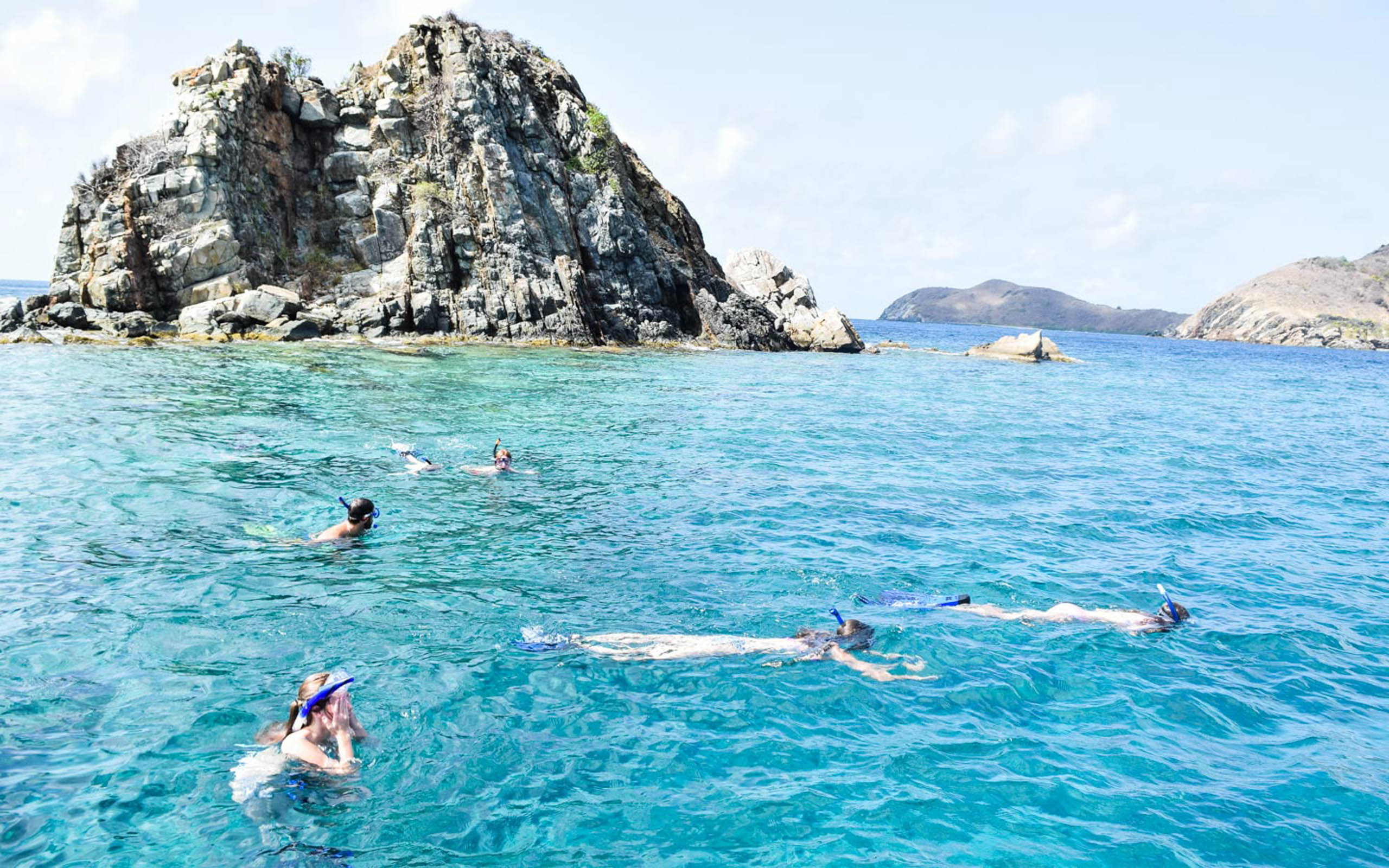A group of people snorkling in the water near a rock.