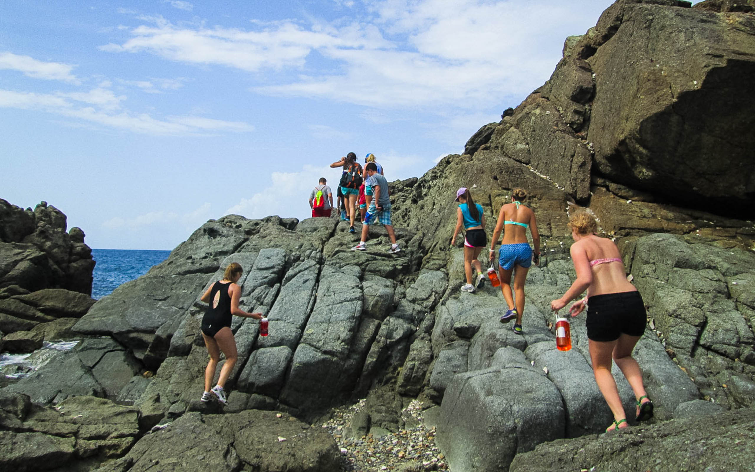 A group of people walking on rocks near the ocean.