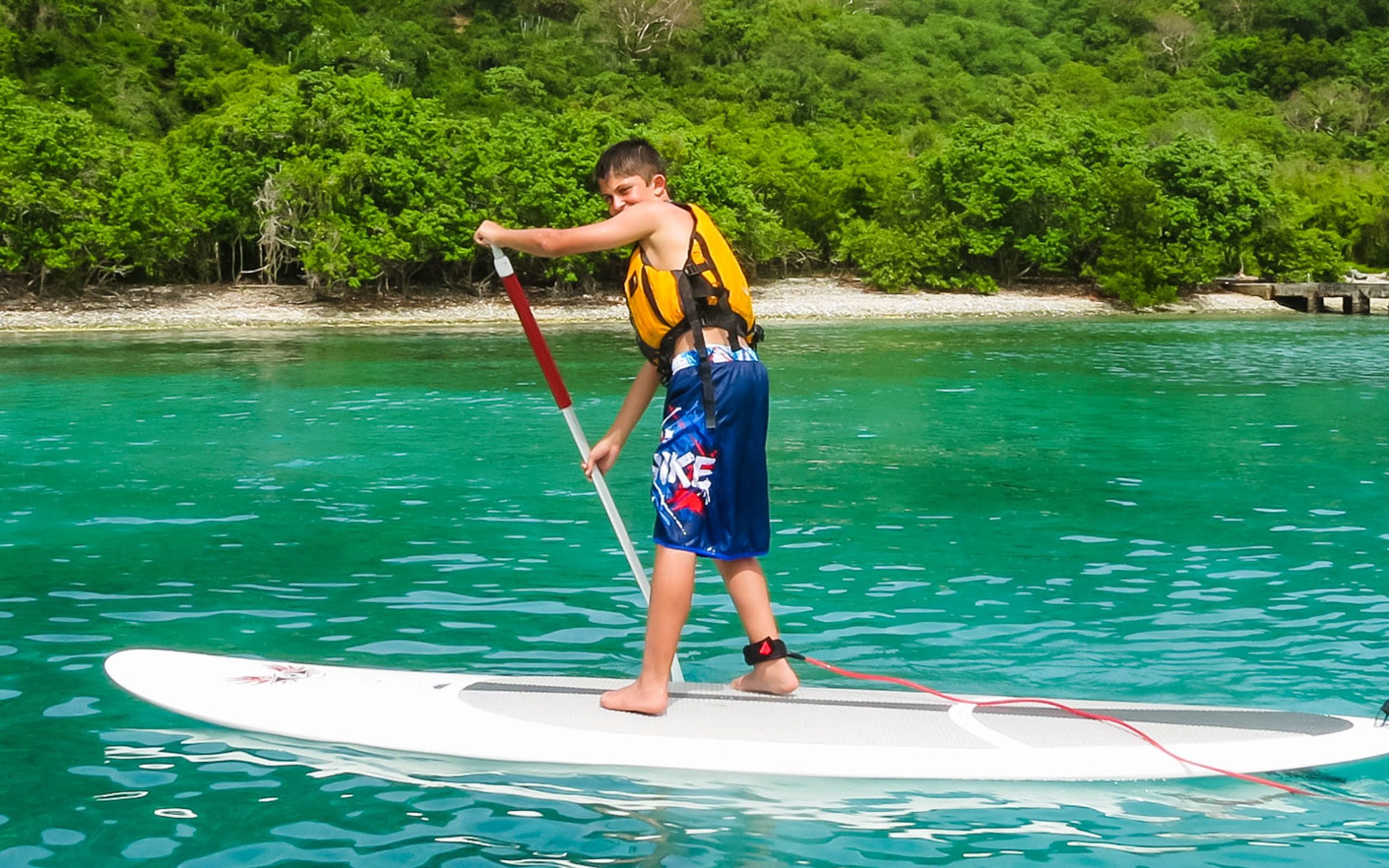 A young man standing on a paddle board in the water.