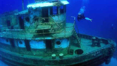 A scuba diver swimming next to a ship.