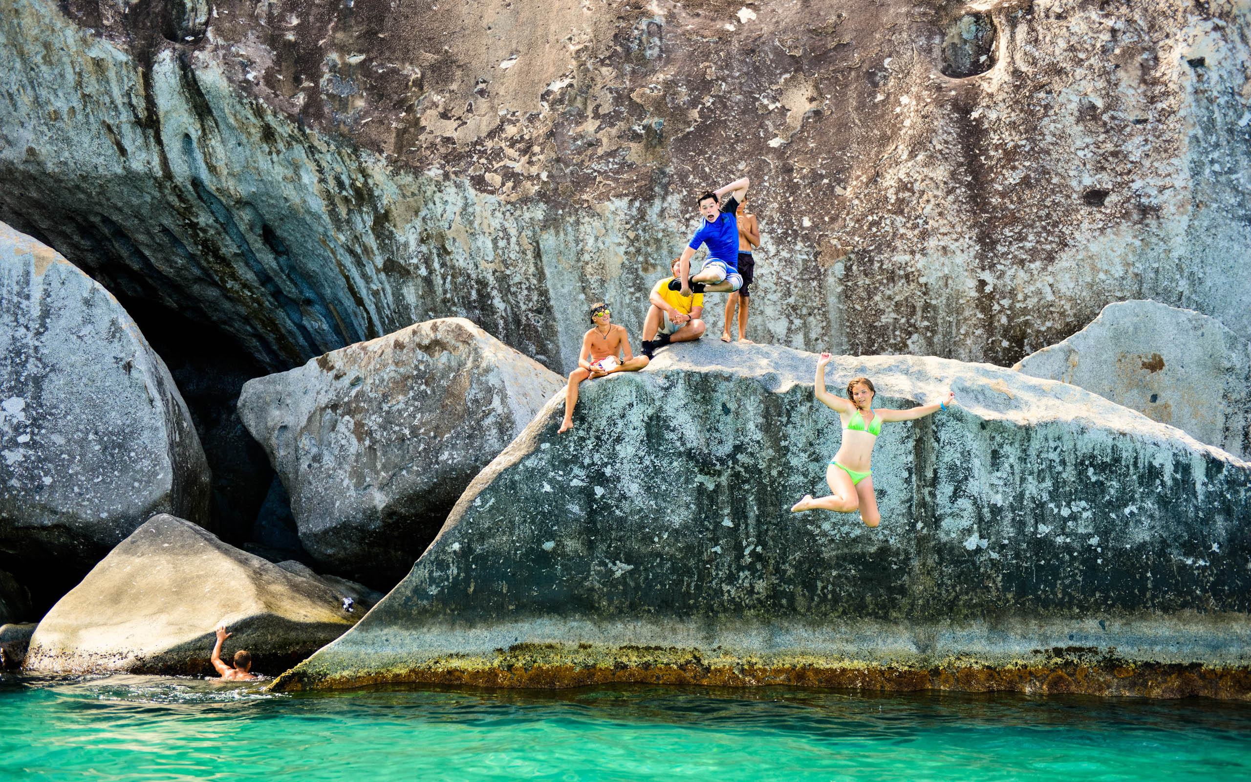 A group of people jumping off of a large rock.