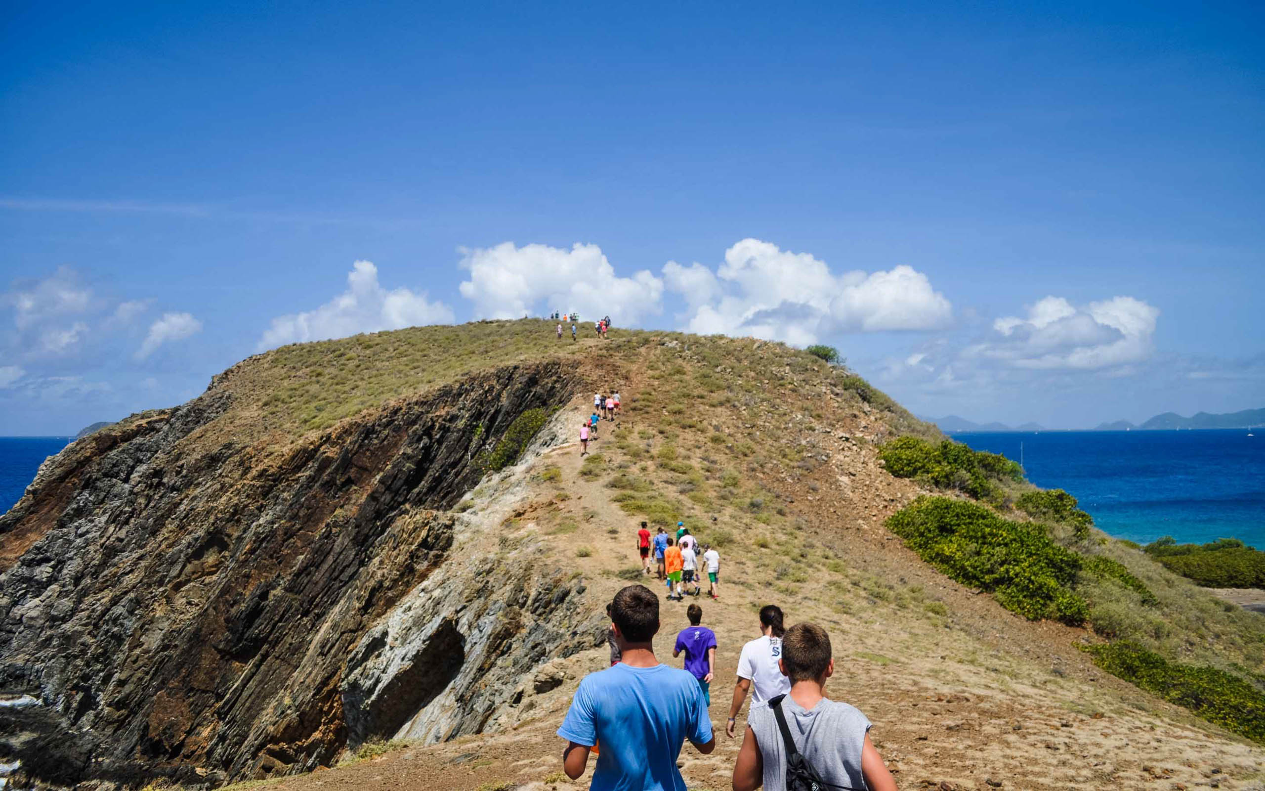 A group of people walking up a hill near the ocean.