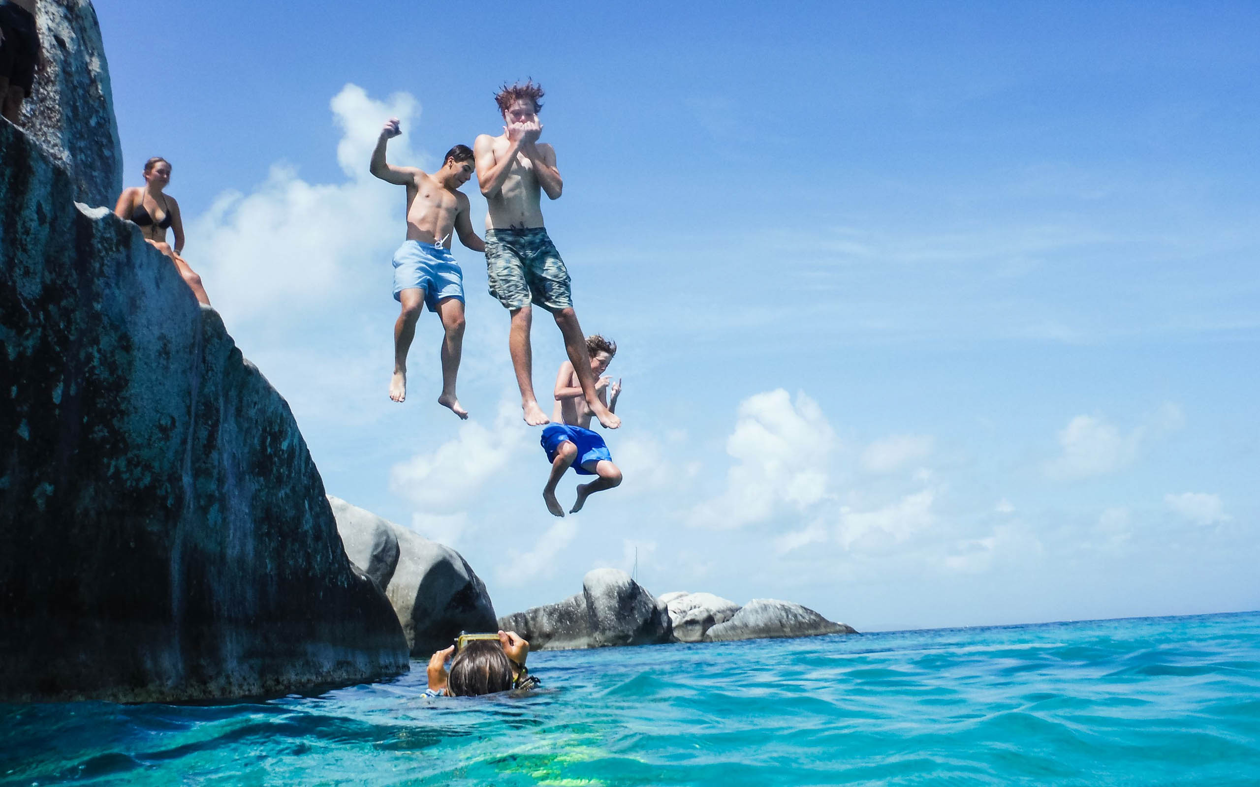 A group of people jumping off a cliff into the ocean.
