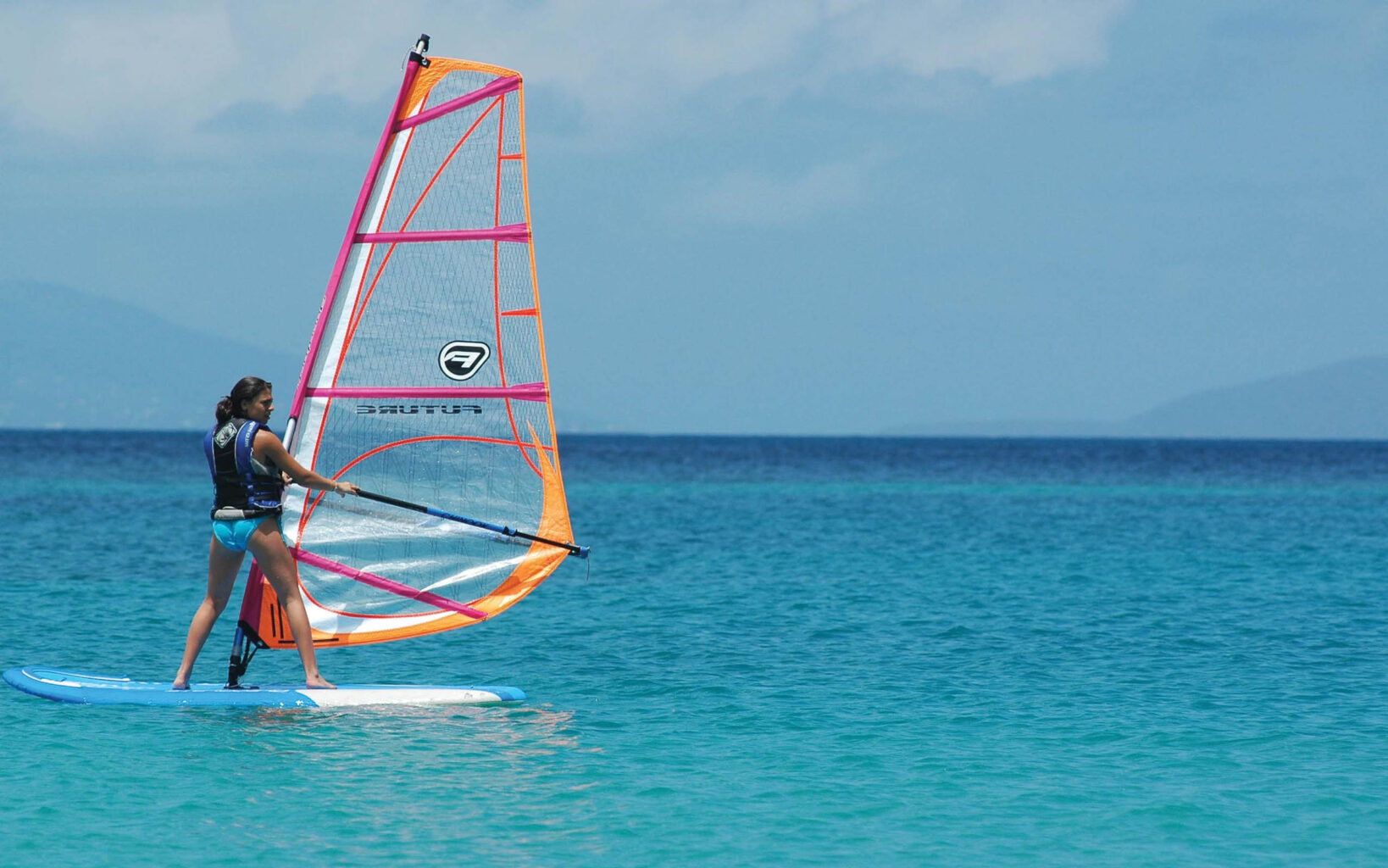 A woman is standing on a windsurf board in the ocean.