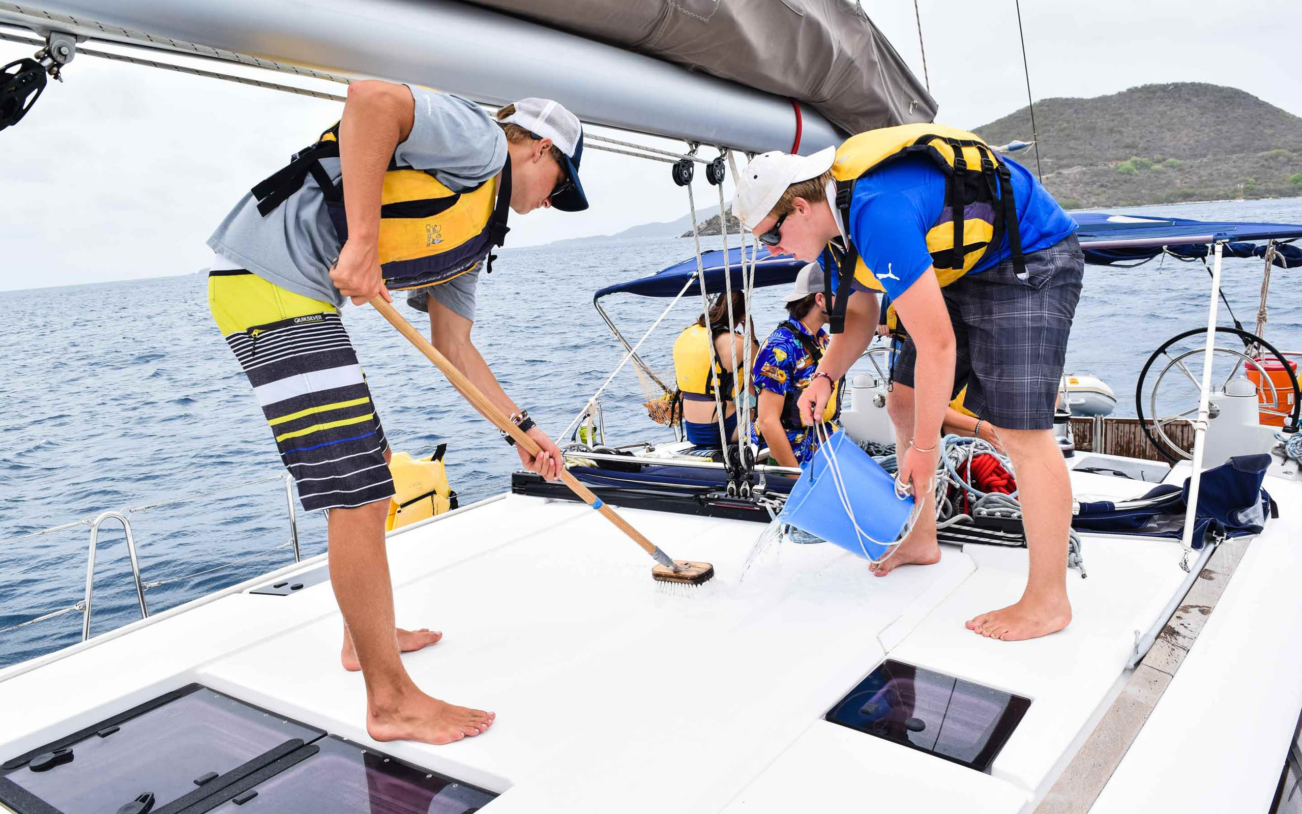 Two men cleaning a sailboat with a broom.