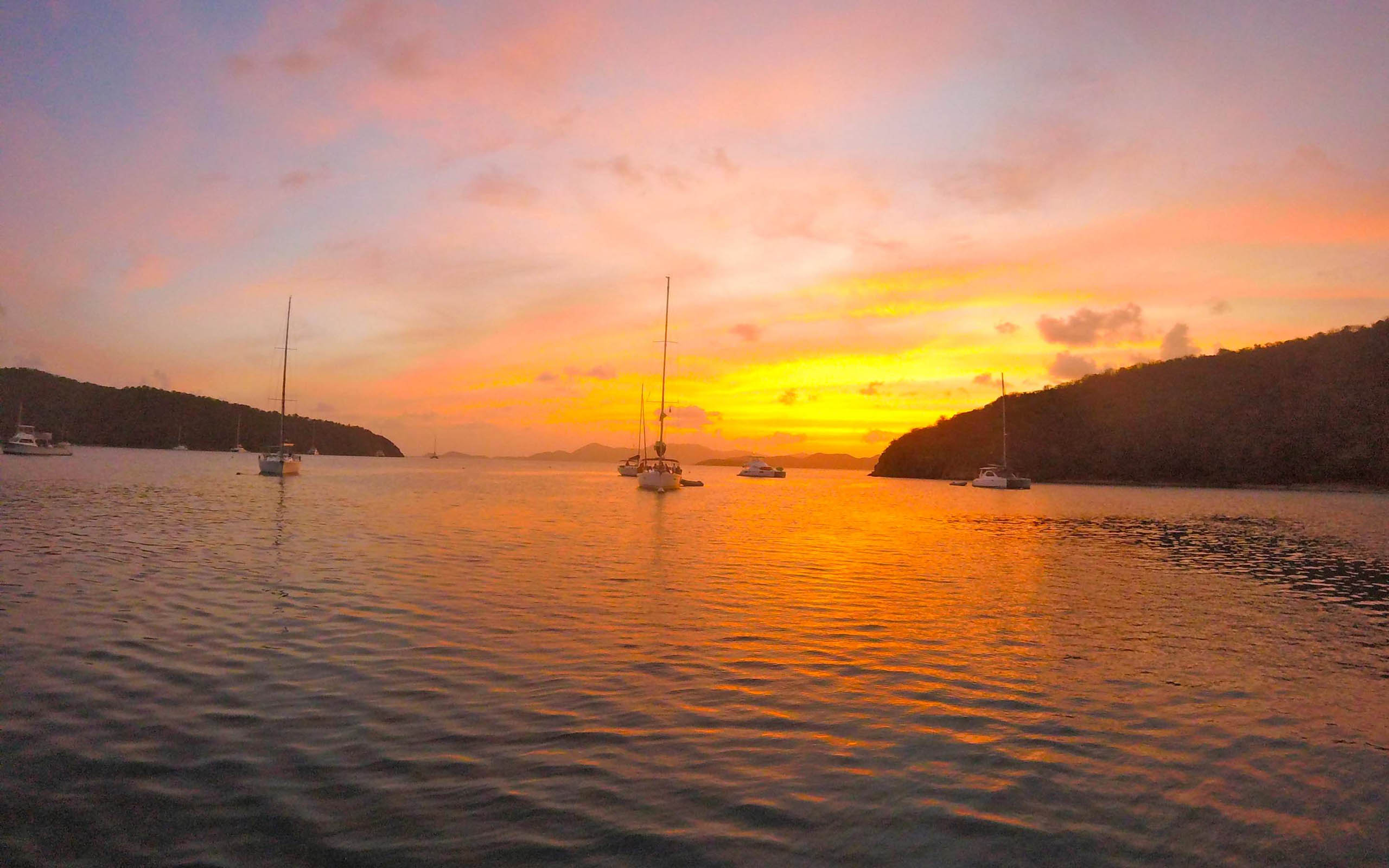 A group of sailboats in a body of water at sunset.