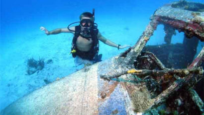 A man scuba diving near an old airplane wreck.