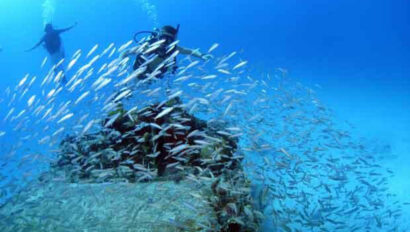 A group of scuba divers in the water near a large rock.