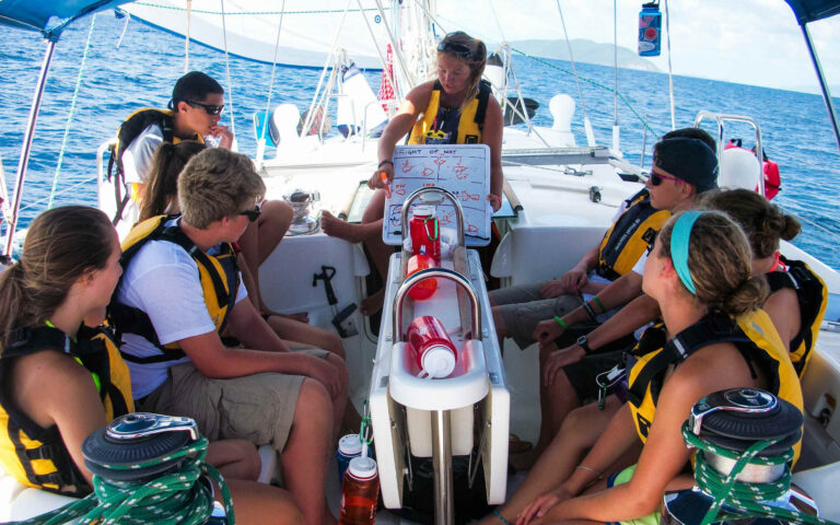 A group of people sitting on the back of a sailboat.