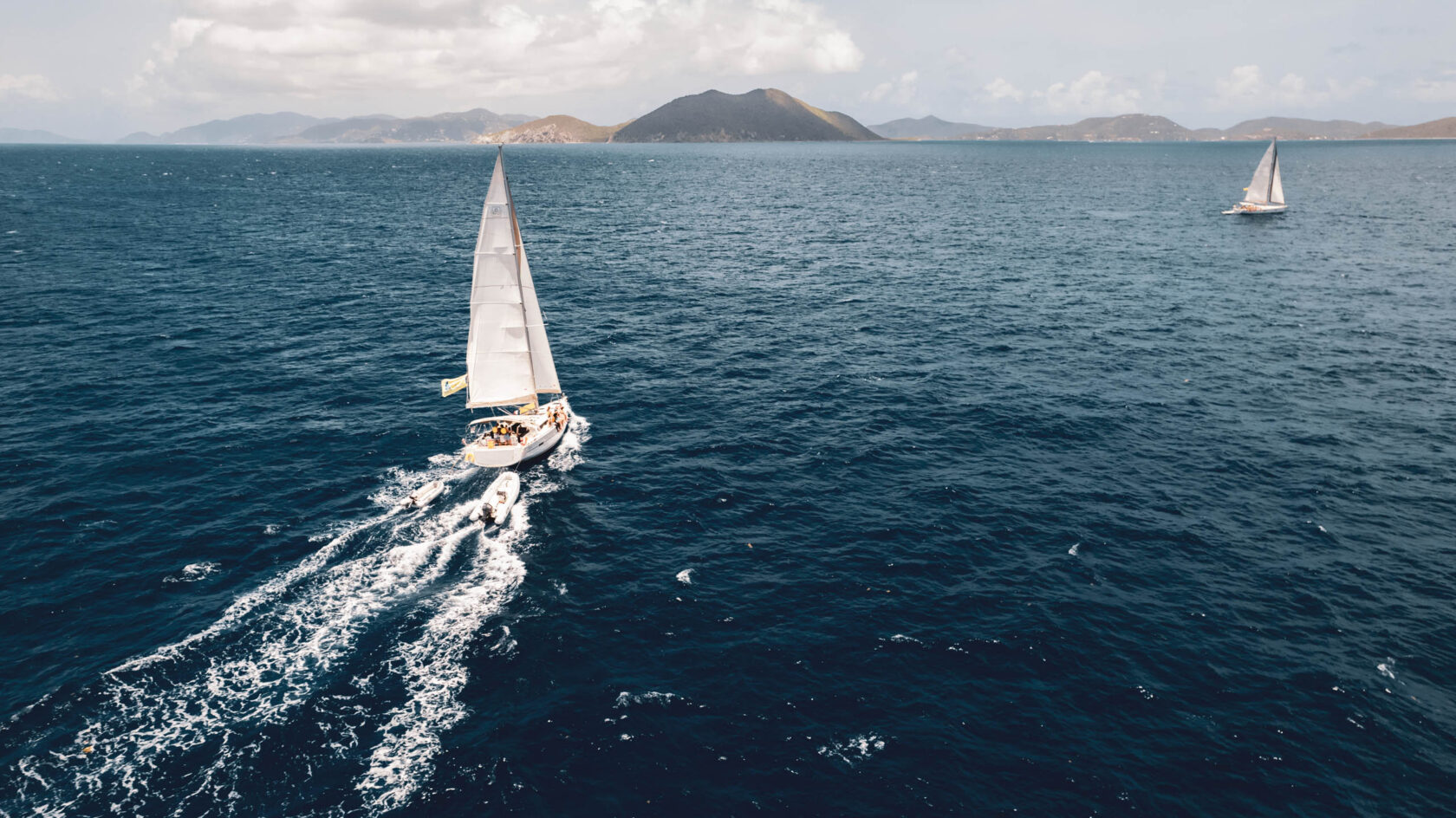 Two sailboats sailing in the ocean with mountains in the background.