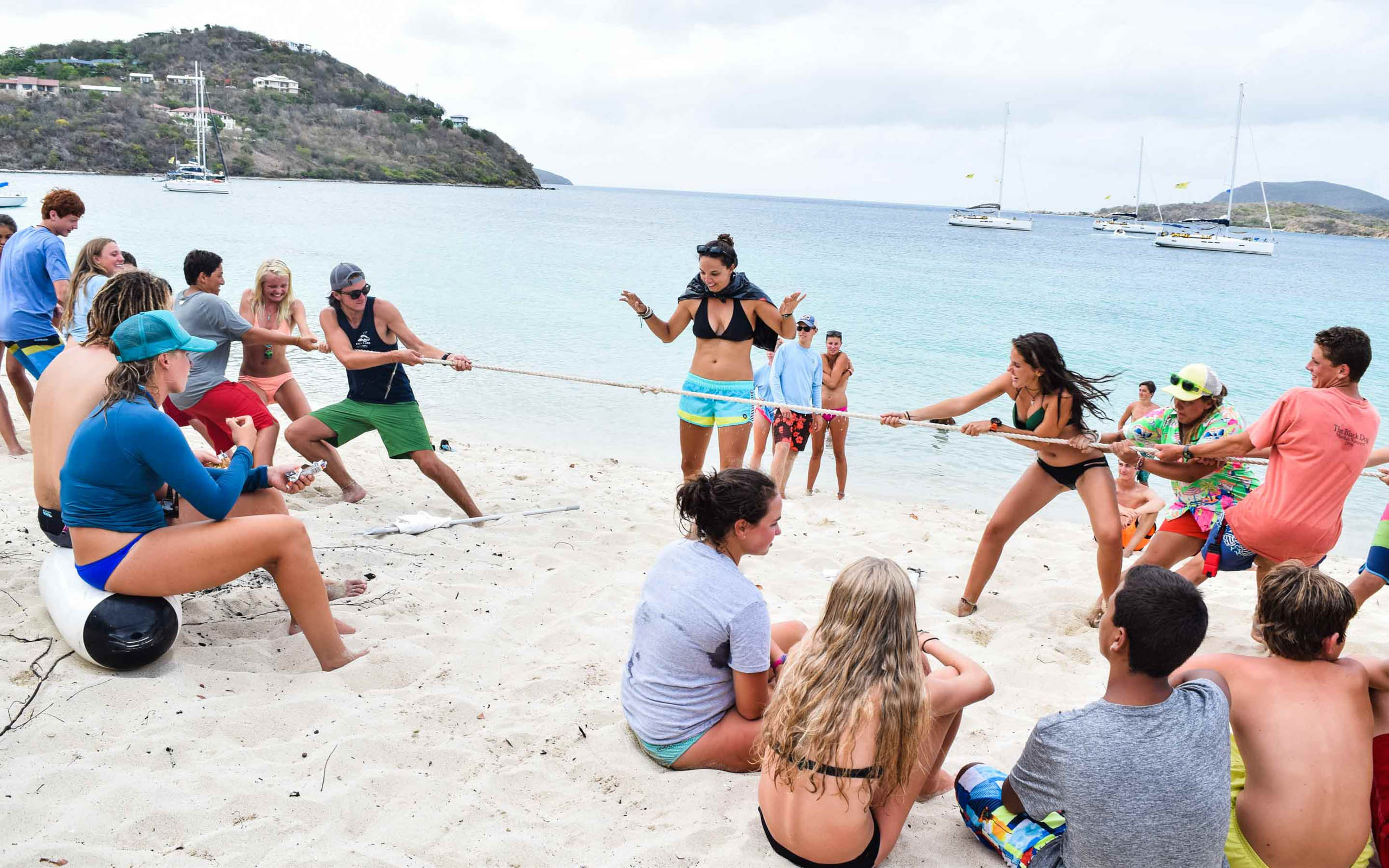A group of people playing tug of war on the beach.