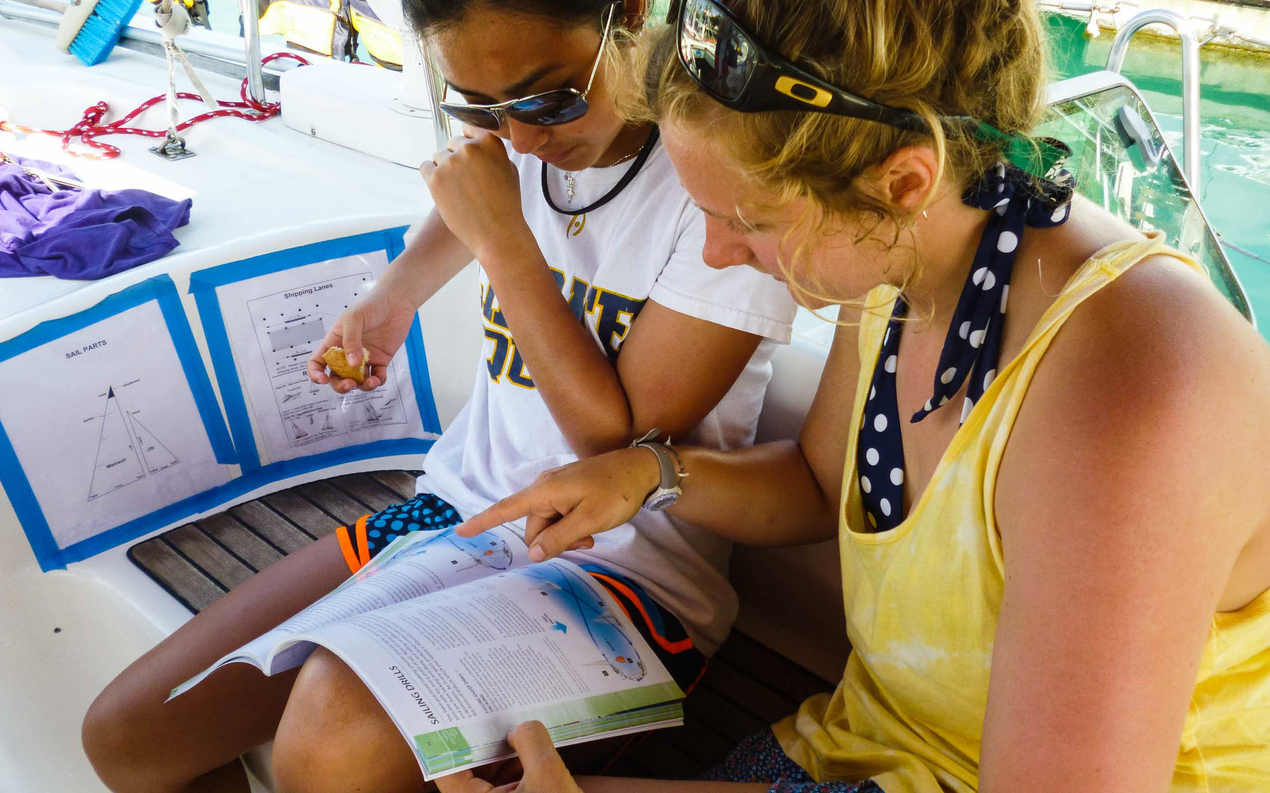 Two women reading a book on a sailboat.