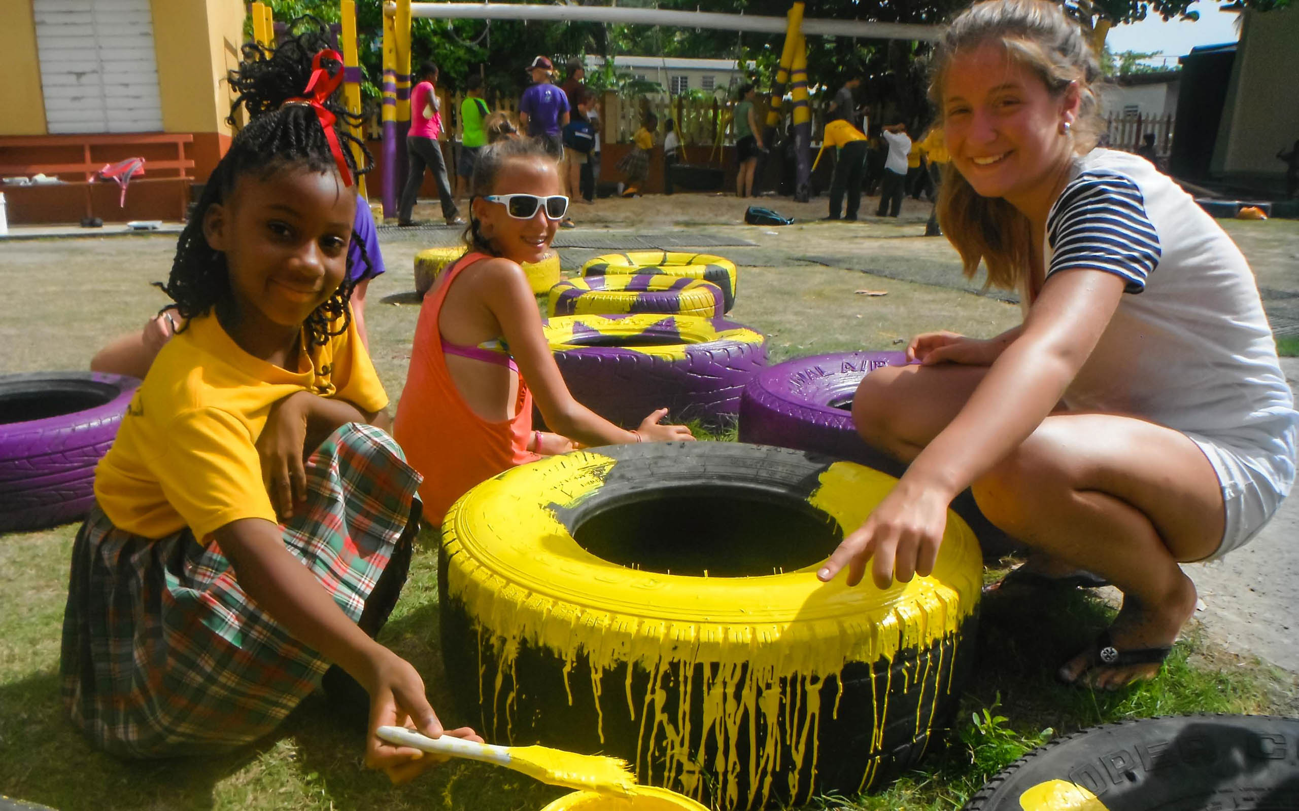 A group of girls painting tires on a grassy area.