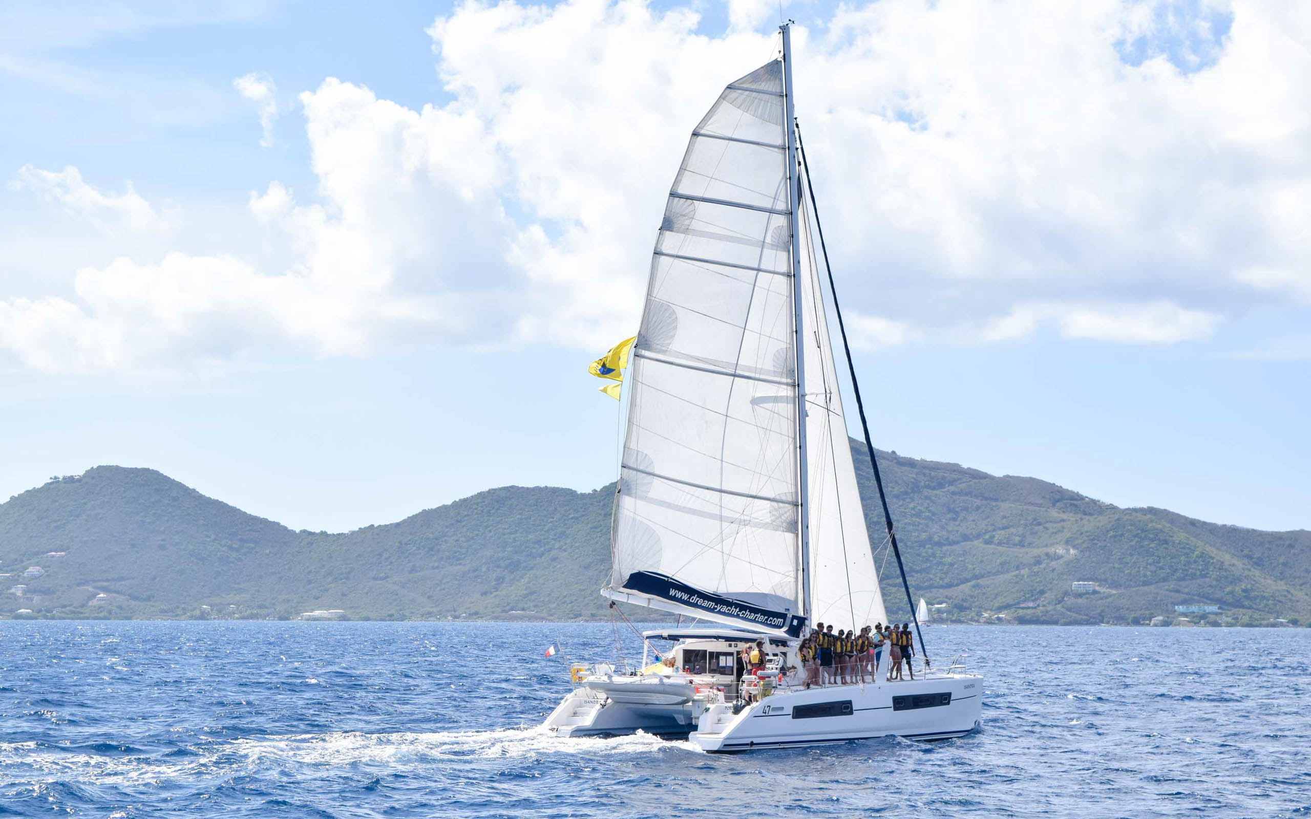 A white catamaran sailing in the ocean with mountains in the background.
