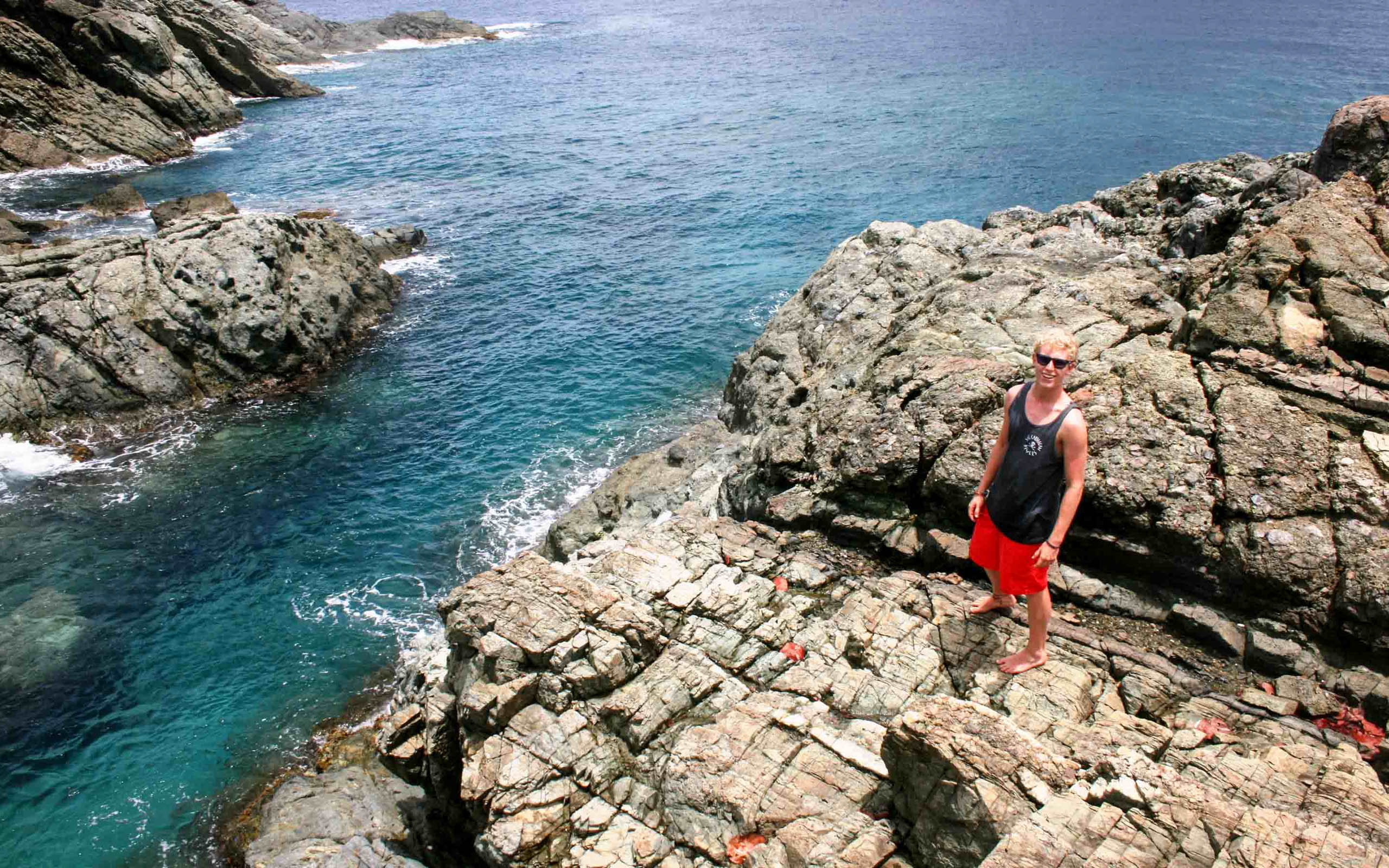 A man standing on a rocky cliff near the ocean.
