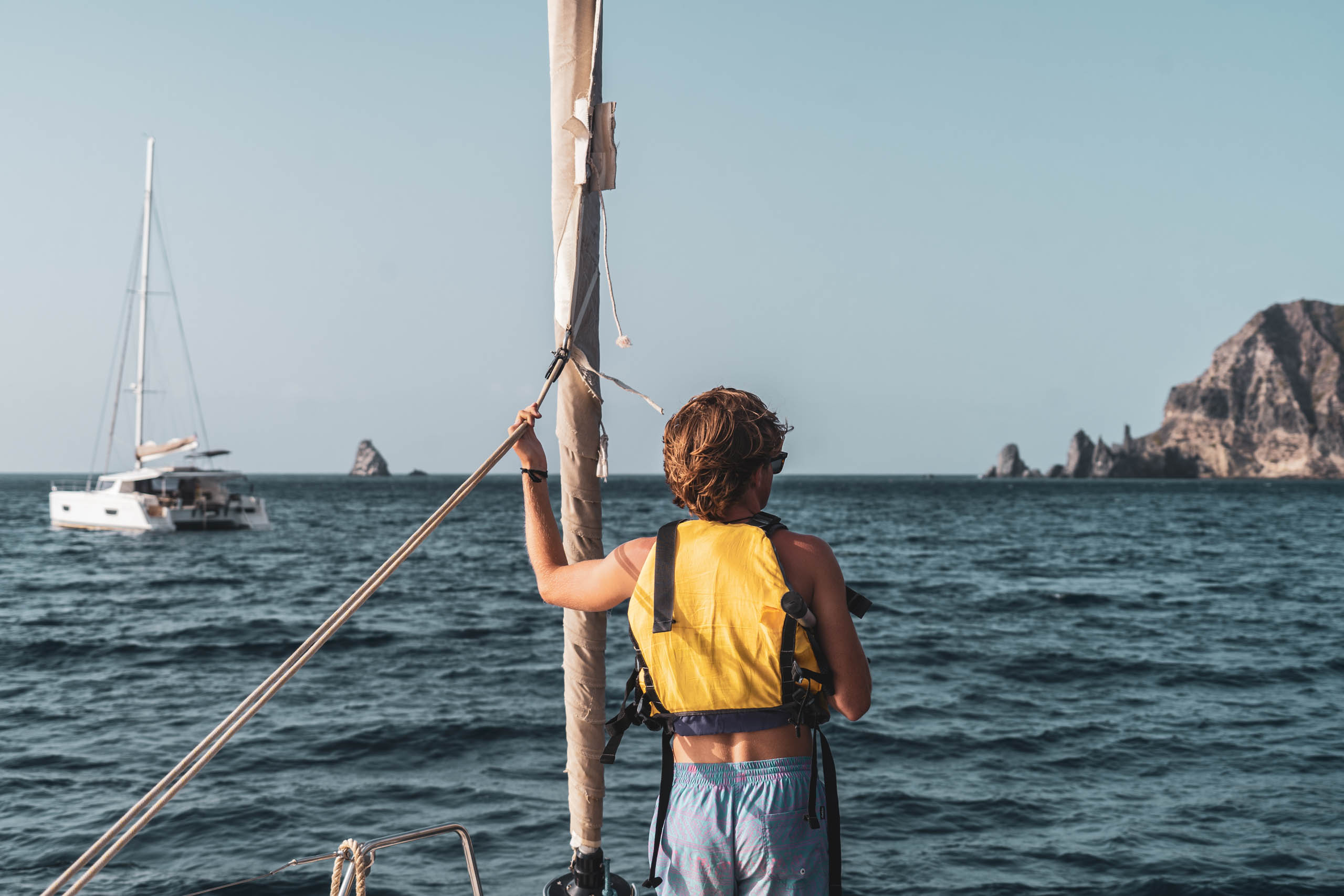 A boy is standing on the bow of a sailboat.