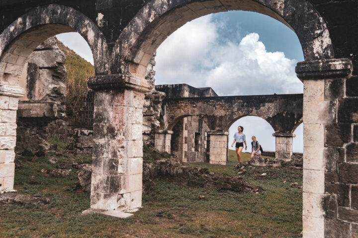 Two people walking through an archway in an old ruins.