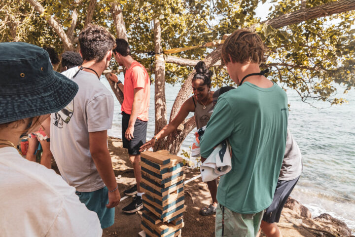 A group of people playing a game of dominoes near the ocean.