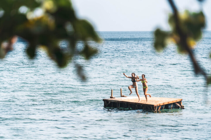 Two people standing on a wooden platform in the ocean.