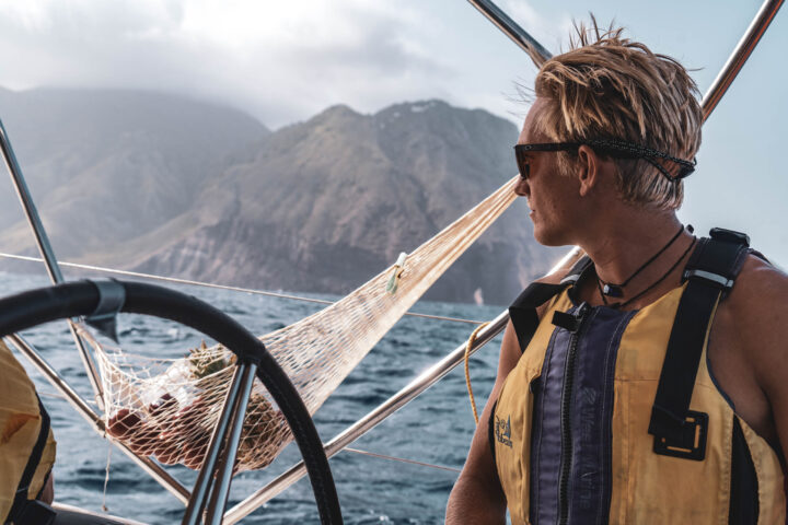 Two people on a sailboat with mountains in the background.