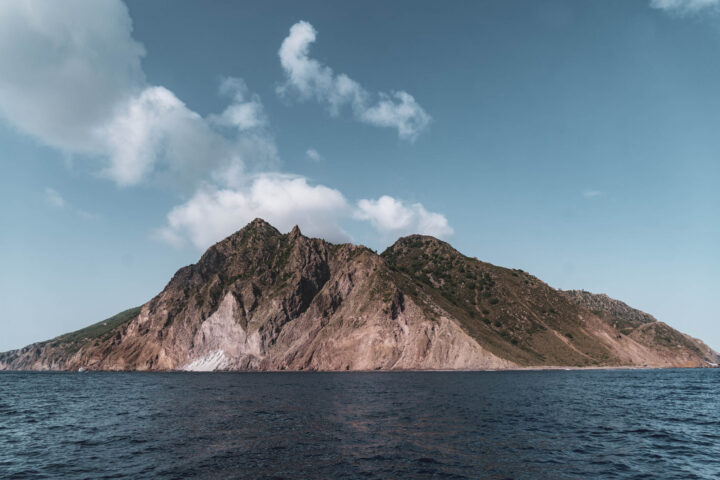 A mountain in the ocean with a cloudy sky.