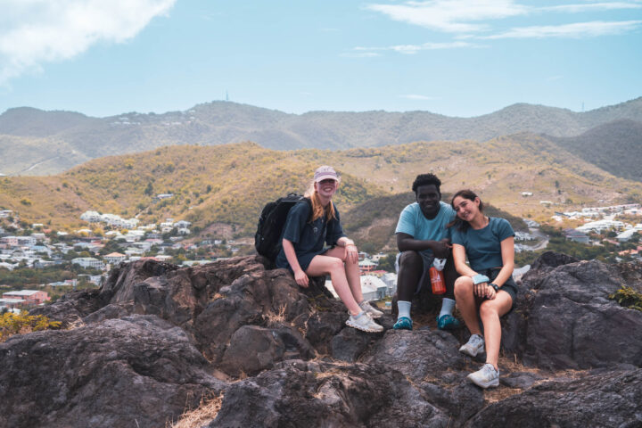Three people sitting on top of a rock with mountains in the background.