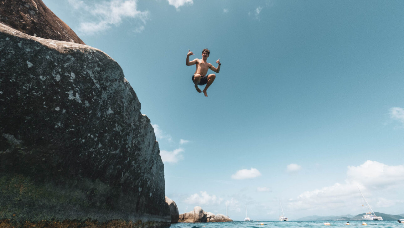 A man jumping off a cliff into the ocean.