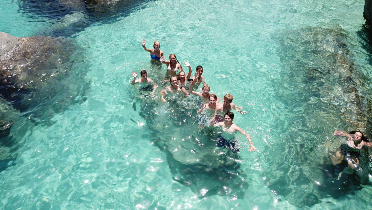Campers swimming in clear water near rocks.