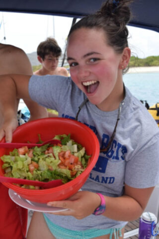 A girl holding a bowl of salad on a boat.