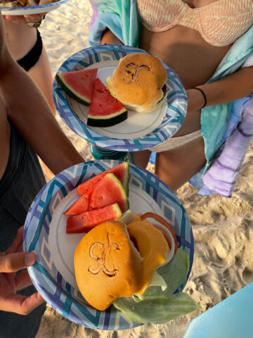 Two campers holding plates with burgers and watermelon on them.